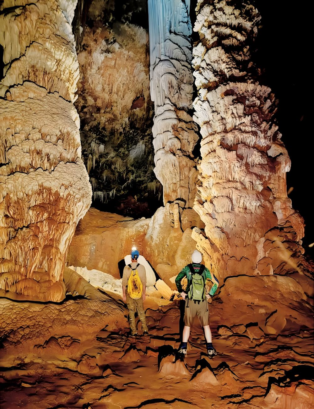 Dois exploradores de capacete entre colunas gigantes de calcário dentro de uma caverna