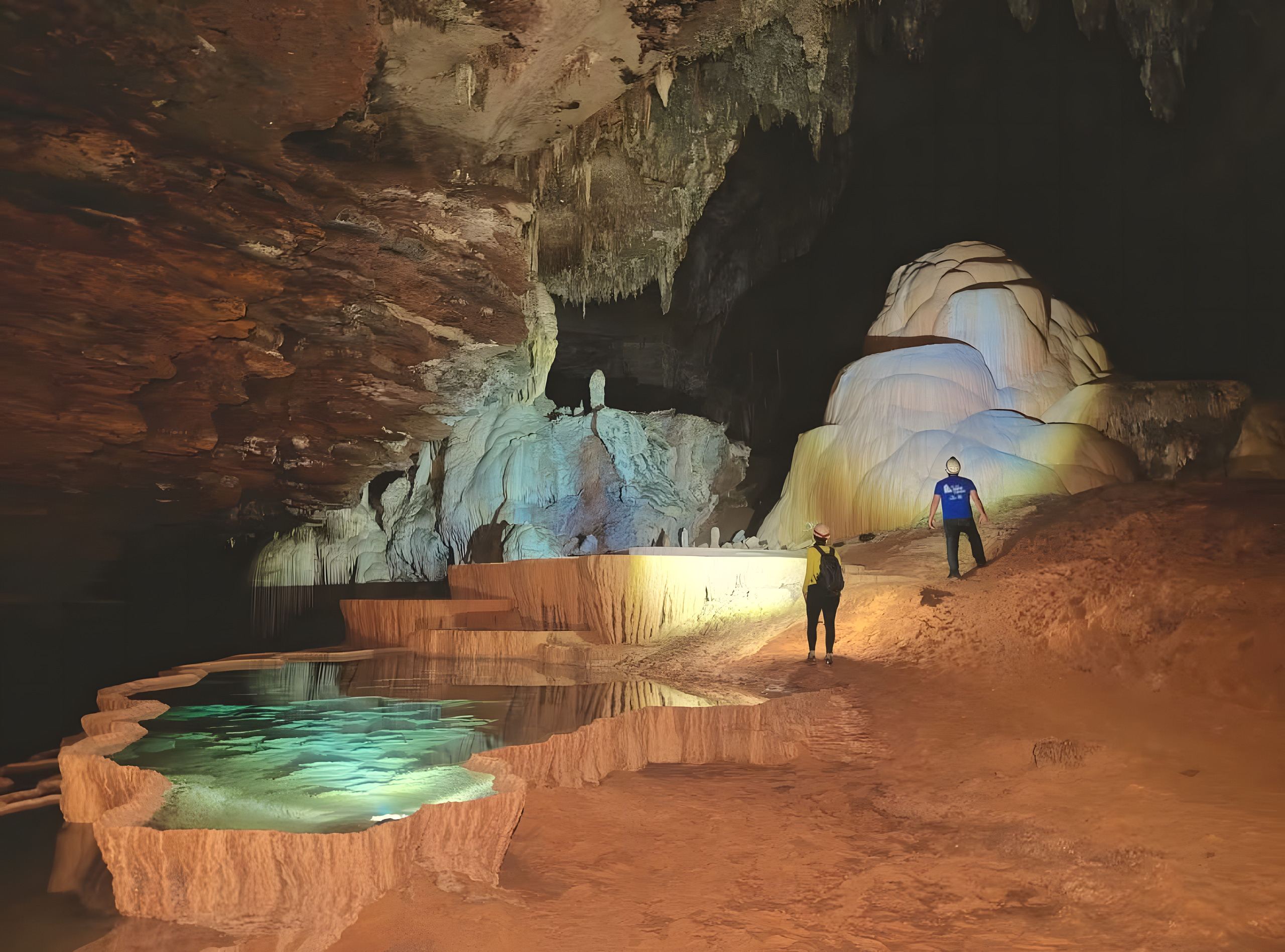 Dois exploradores de capacete dentro de uma caverna, entre formações de pedra iluminadas