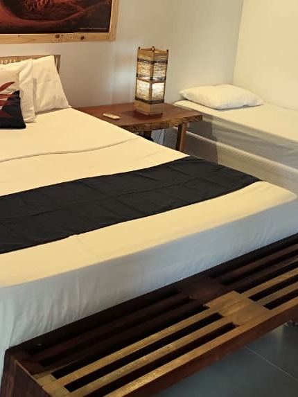 Abajur de fibra sobre o criado-mudo de madeira, ao lado da cama e de uma cama de solteiro